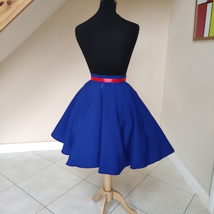 May include: A royal blue circle skirt with a red satin waistband. The skirt is on a dress form and is photographed against a white wall.