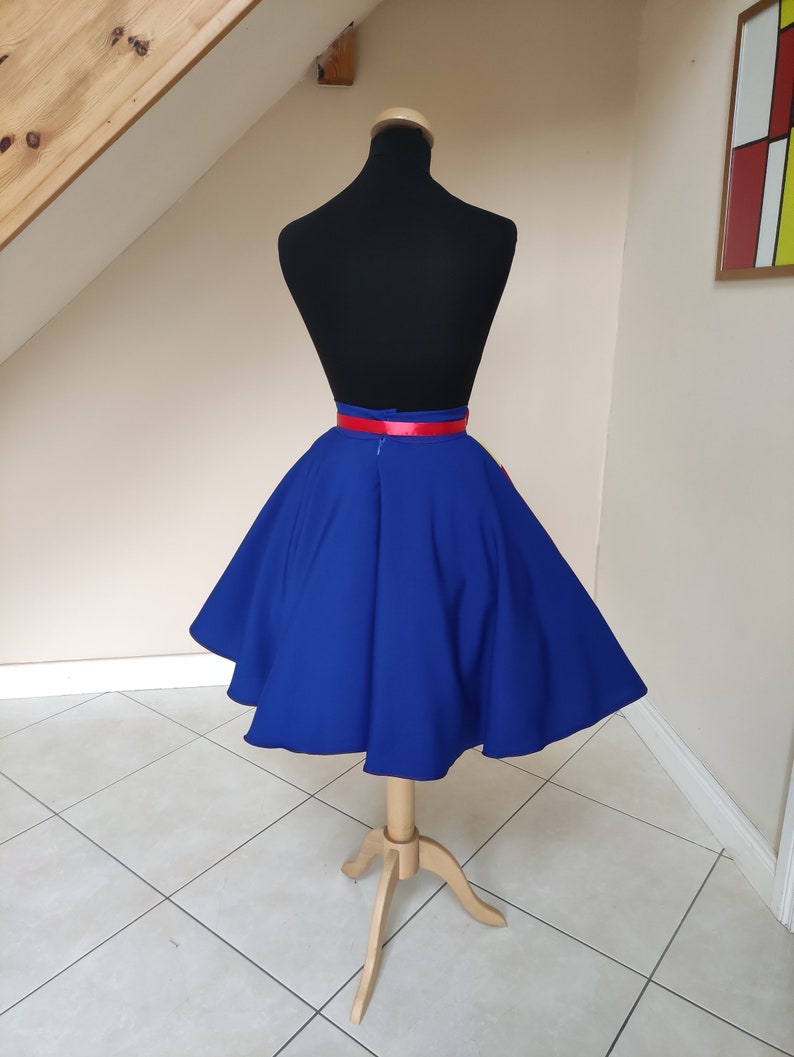 May include: A royal blue circle skirt with a red satin waistband. The skirt is on a dress form and is photographed against a white wall.