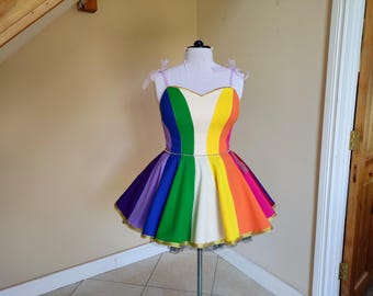 May include: A rainbow-colored dress with a white bodice and a full skirt. The skirt is made of six panels of fabric, each a different color of the rainbow. The dress is on a mannequin.