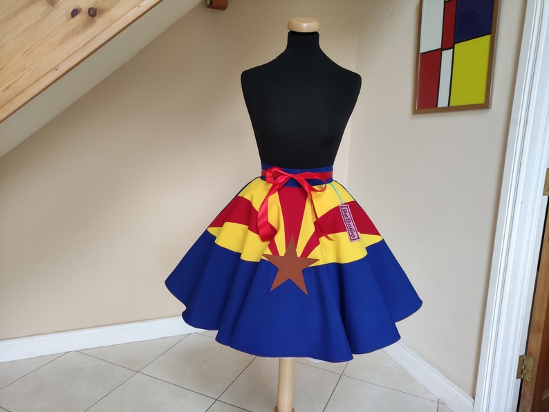 May include: A blue, red and yellow circle skirt with a red ribbon tied around the waist. The skirt features the Arizona state flag design with a brown star in the centre. The skirt has a tag that says "The Bag Lady".