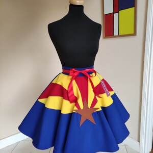May include: A blue, yellow and red circle skirt with the Arizona state flag design. The skirt has a red ribbon tied at the waist and a "Retago" tag.
