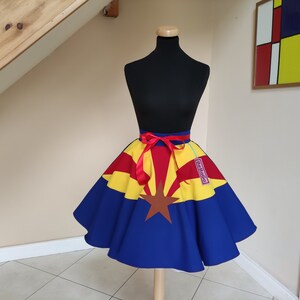 May include: A blue, yellow and red circle skirt with a red ribbon belt. The skirt is decorated with the Arizona state flag. The skirt is on a white mannequin.