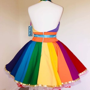 May include: A rainbow-colored dress with a halter neckline and a full skirt. The dress has a gold trim and a white petticoat. The dress is labeled "BeBoGo".