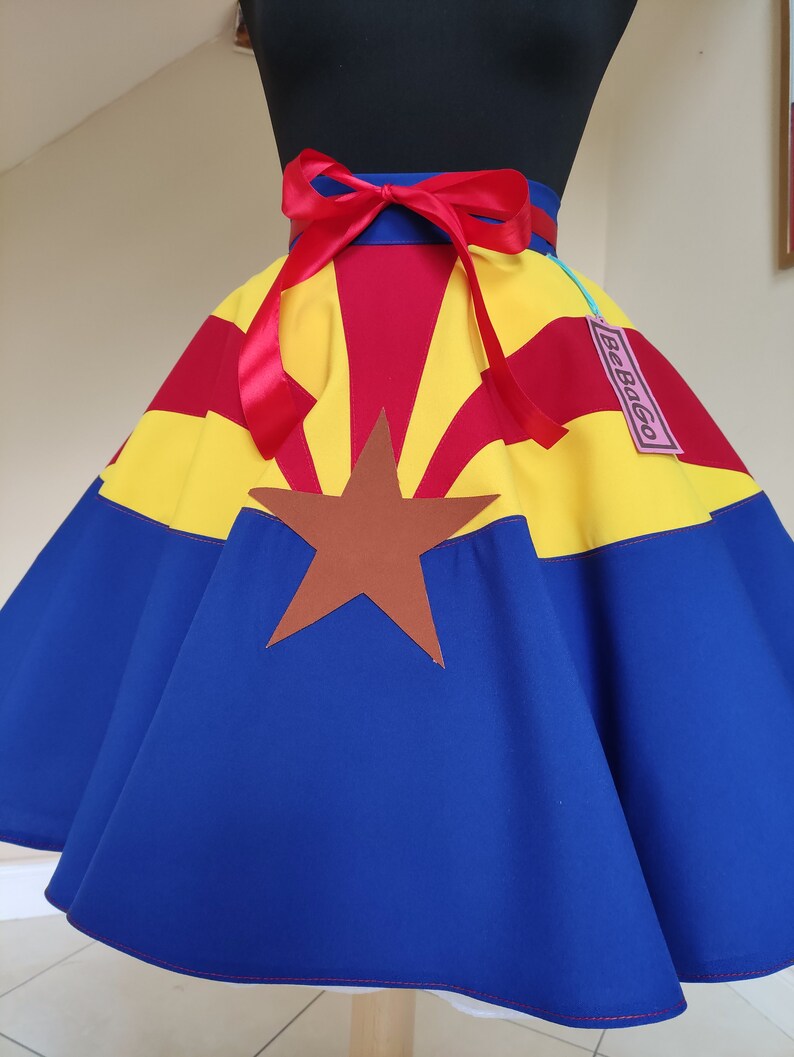 May include: A blue, red and yellow skirt with a brown star in the centre. The skirt is a circle skirt with a red ribbon tied around the waist. The tag on the skirt says "BeBopGo".