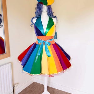 May include: A rainbow-colored dress with a matching hat. The dress has a fitted bodice and a full skirt with a tulle underskirt. The hat is a beret style with a pom-pom on top. The dress is on a white mannequin.