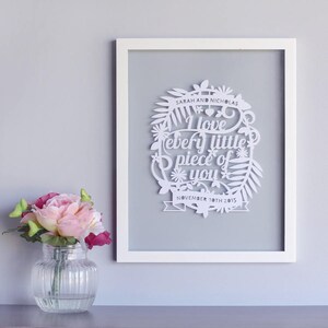 Puede incluir: Arte de papel cortado en blanco enmarcado en un marco blanco. El arte presenta un c&iacute;rculo con un dise&ntilde;o floral y el texto "I love every little piece of you" con la fecha "November 10th 2015" debajo. Los nombres "Sarah and Nicholas" est&aacute;n en la parte superior del c&iacute;rculo.