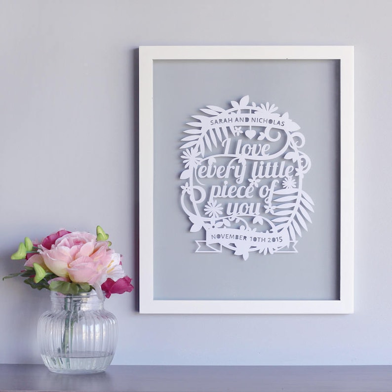 Puede incluir: Arte de papel cortado en blanco enmarcado en un marco blanco. El arte presenta un c&iacute;rculo con un dise&ntilde;o floral y el texto "I love every little piece of you" con la fecha "November 10th 2015" debajo. Los nombres "Sarah and Nicholas" est&aacute;n en la parte superior del c&iacute;rculo.
