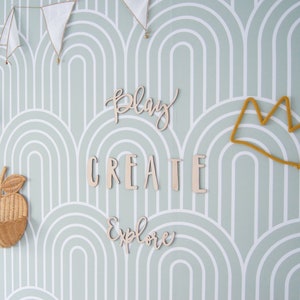 May include: A light green wall with a white and light green arched pattern. The wall is decorated with wooden cutouts that say "Play", "Create", and "Explore". There is also a yellow yarn crown hanging on the wall.