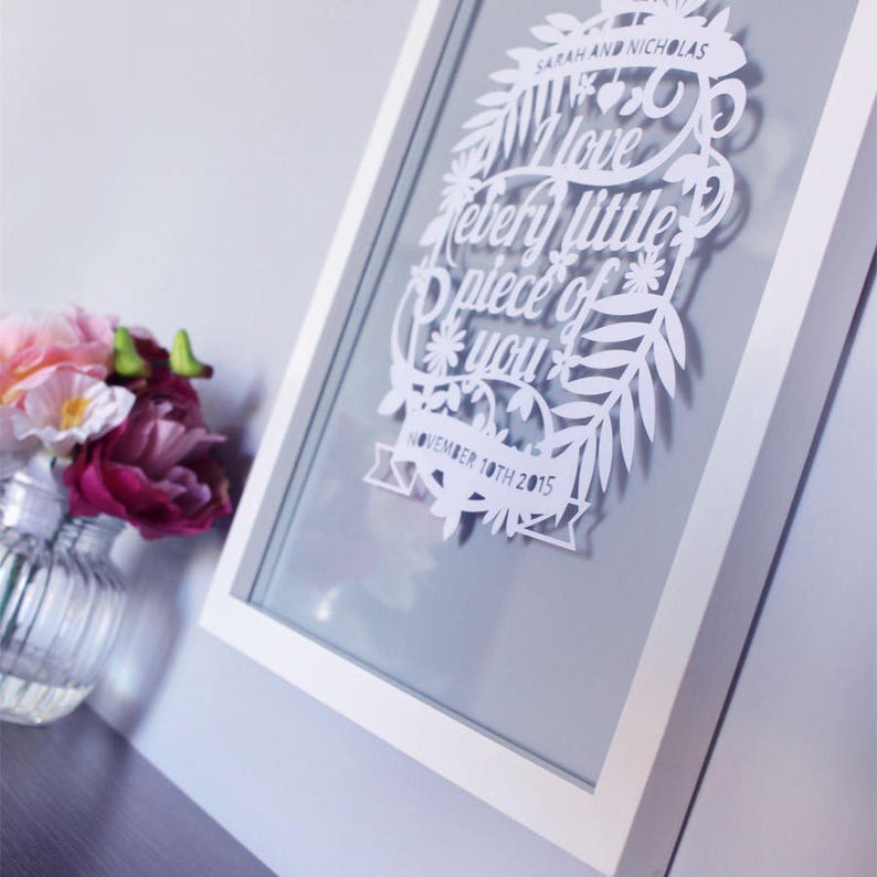 Puede incluir: Arte de corte de papel blanco enmarcado en un marco blanco. El arte presenta un dise&ntilde;o floral con el texto "Amo cada peque&ntilde;a parte de ti" y la fecha "10 de noviembre de 2015".