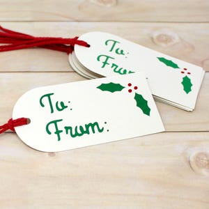May include: White gift tags with red string, featuring the text "To: From:" in green script. Each tag has a holly and berry design in green and red. A stack of tags is visible.