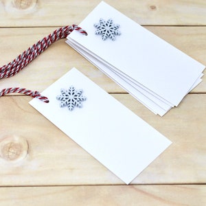 May include: A stack of white gift tags with silver snowflake embellishments and red and silver twine.