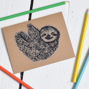 May include: A brown card with a black and white illustration of a sloth on it. The card is surrounded by colored pencils on a white wooden surface.