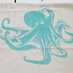 May include: A teal blue octopus printed on a white cotton tea towel.