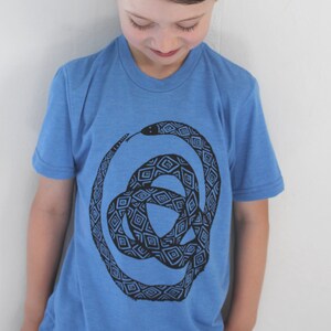 May include: A young person wearing a blue t-shirt with a black and white geometric snake design.