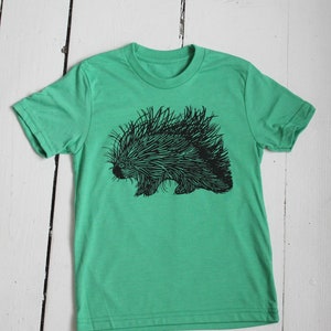 May include: A green t-shirt with a black and white illustration of a porcupine.