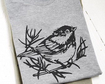 May include: A gray t-shirt with a black and white illustration of a bird perched on a branch.