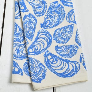 May include: A white kitchen towel with a blue oyster pattern. The oysters are drawn in a simple, stylized design.