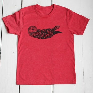 May include: Red t-shirt with a black and white illustration of a sea otter.
