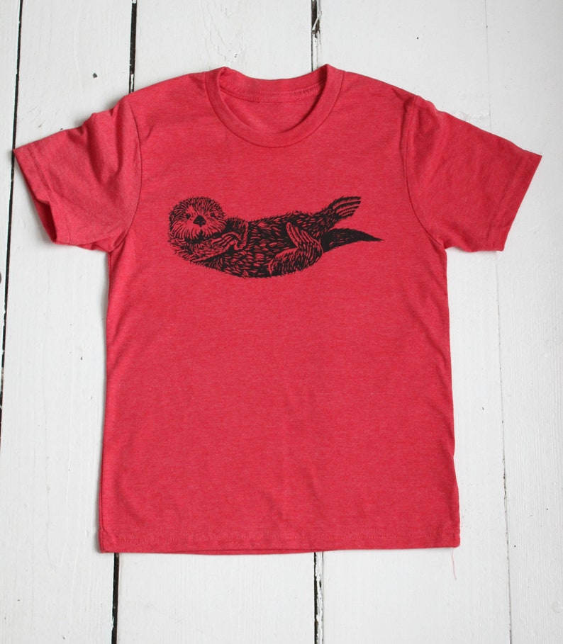 May include: Red t-shirt with a black and white illustration of a sea otter.