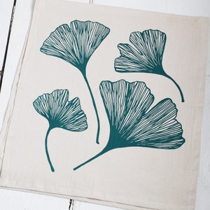 Op de afbeelding: Een witte theedoek met een teal ginkgo-bladontwerp. De bladeren zijn gestileerd en hebben een gedetailleerd lijnenpatroon.