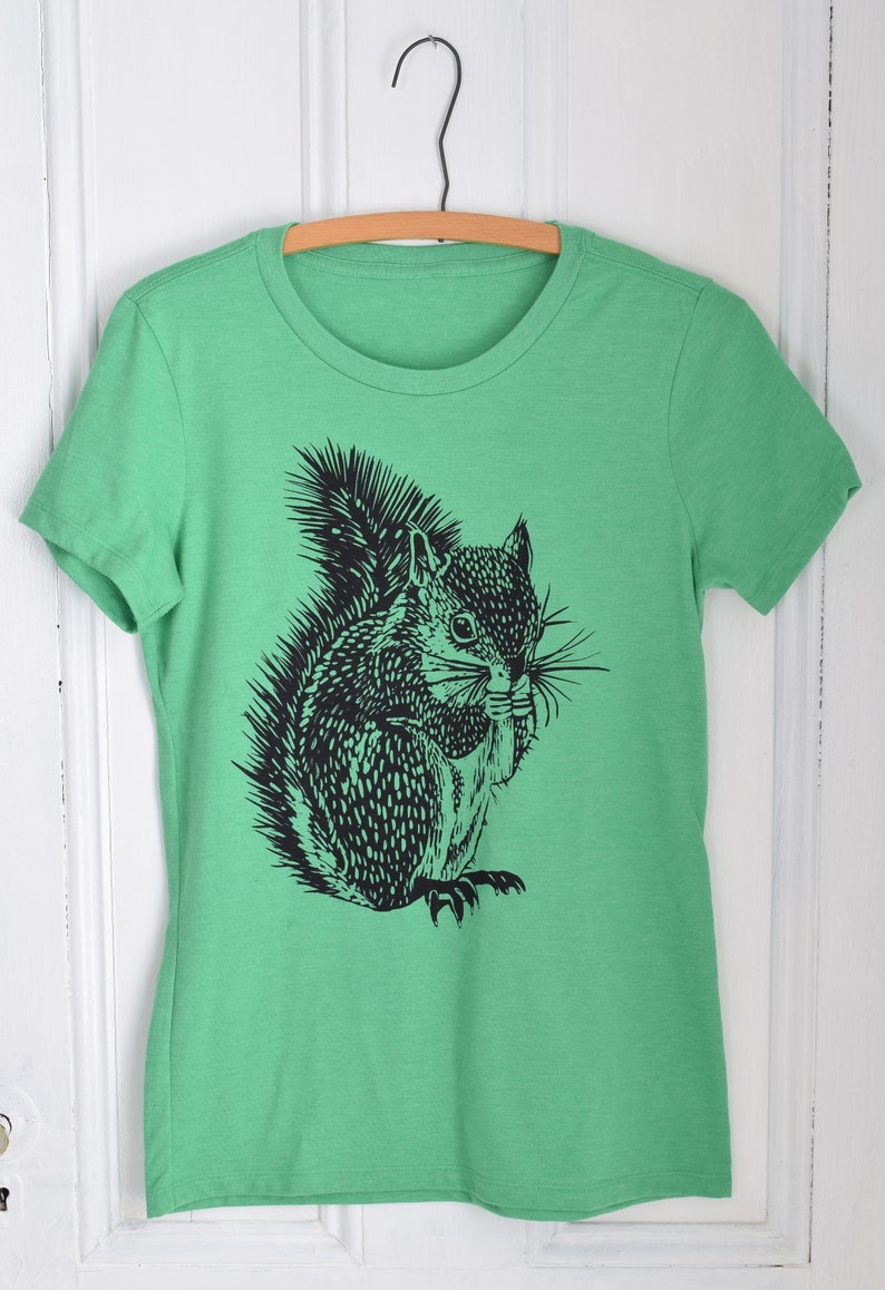 May include: A green t-shirt with a black and white illustration of a squirrel holding a nut in its mouth.