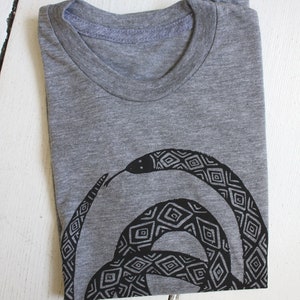 May include: A gray t-shirt with a black and white geometric snake design printed on the front.