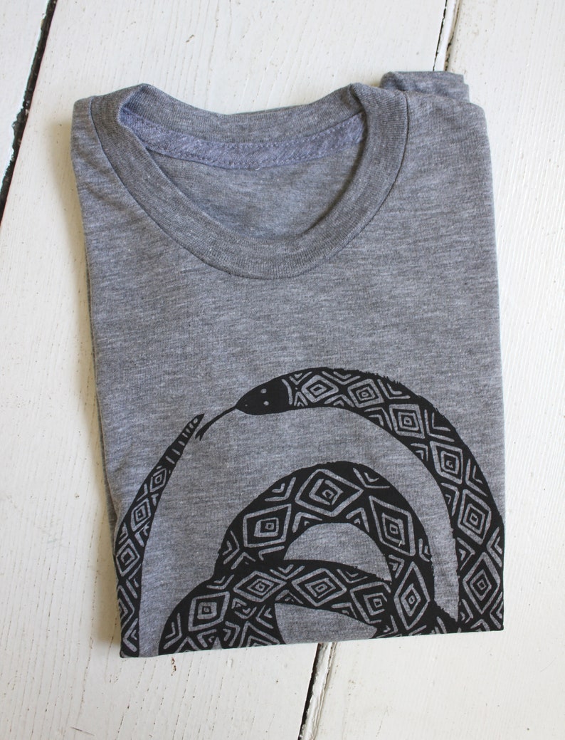 May include: A gray t-shirt with a black and white geometric snake design printed on the front.