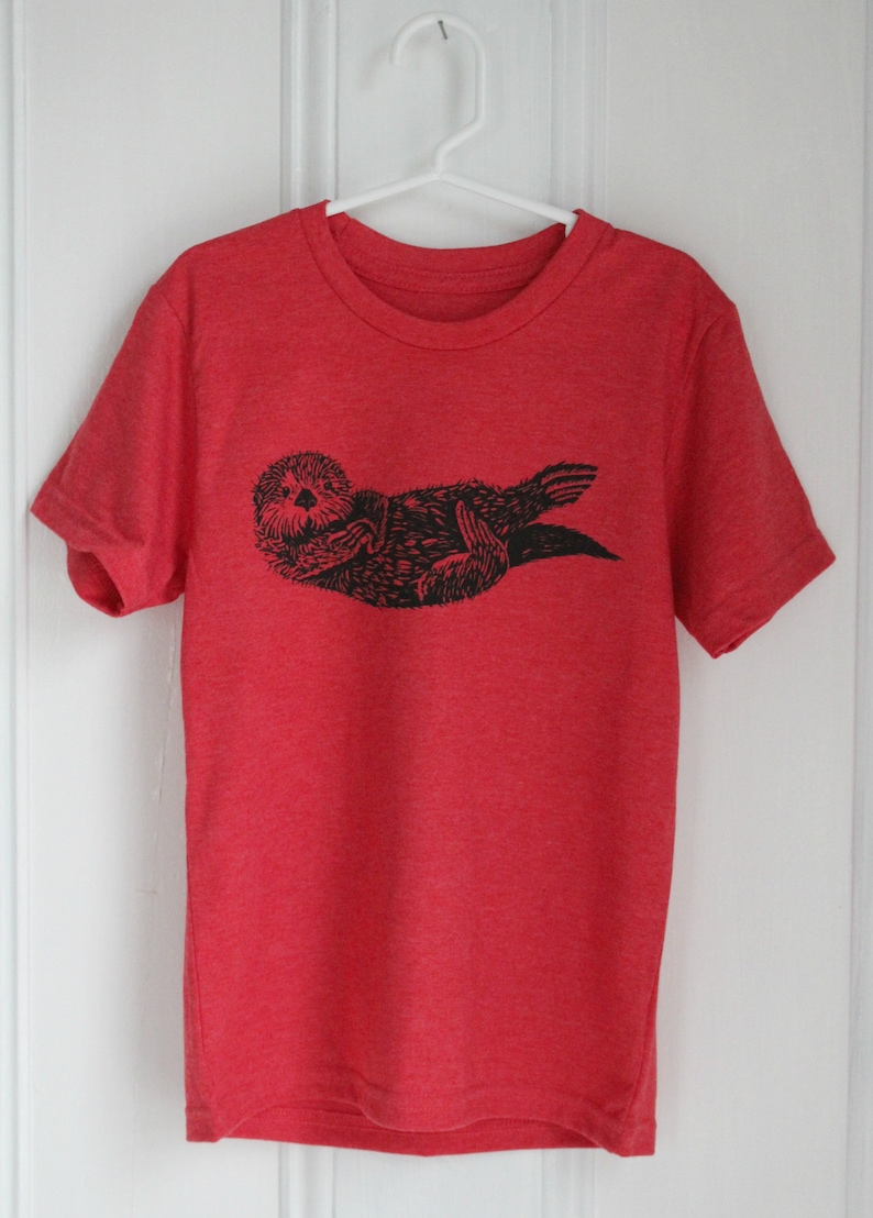 May include: Red t-shirt with a black and white graphic print of a sea otter.