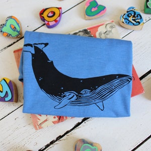 May include: A blue t-shirt with a black whale graphic. The shirt is surrounded by colorful wooden hearts with letters painted on them.