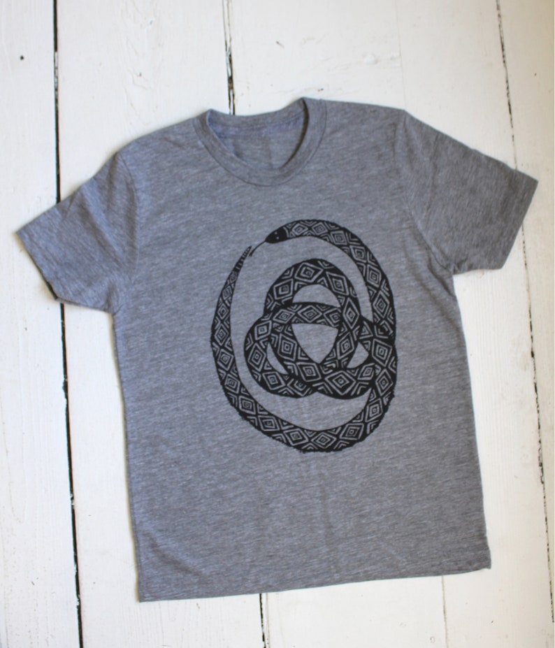 May include: A gray t-shirt with a black and white graphic print of a snake coiled in a circle. The snake is patterned with geometric shapes.