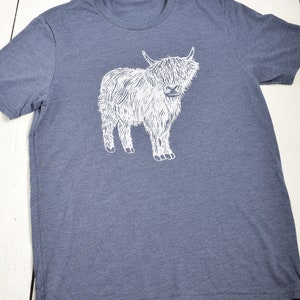 May include: A heather blue t-shirt with a white graphic of a Highland cow.