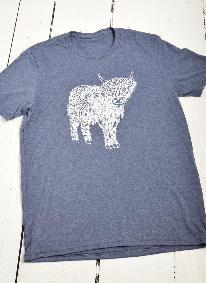 May include: A heather blue t-shirt with a white graphic of a Highland cow.