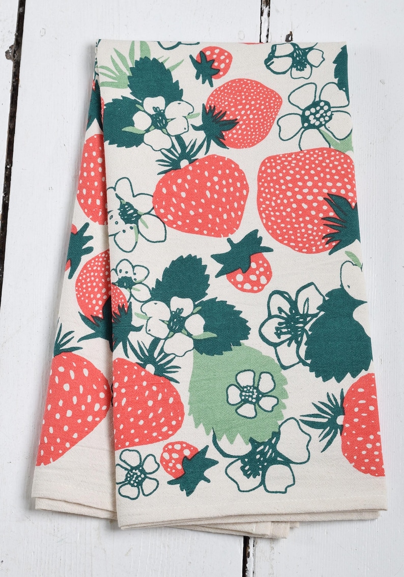 May include: Two folded tea towels with a white background and a repeating pattern of red strawberries, green leaves, and white flowers.
