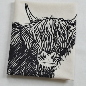 May include: Black and white illustration of a Highland cow's head with a fluffy mane and a detailed snout. The image is printed on a cream-colored fabric.