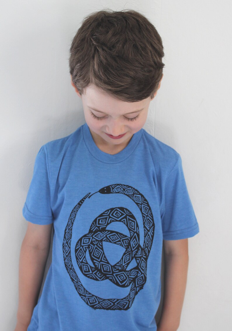 May include: A young person wearing a blue t-shirt with a black and white geometric snake design.