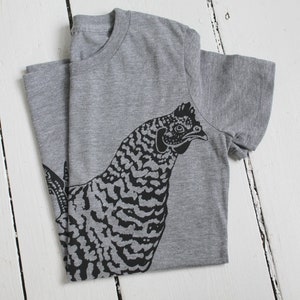 May include: A gray t-shirt with a black and white illustration of a chicken on the front.