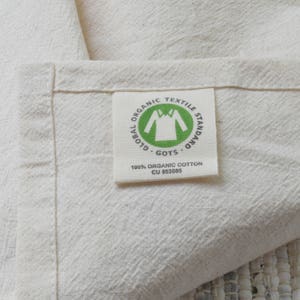 May include: A white fabric label with green text that reads "Global Organic Textile Standard GOTS 100% Organic Cotton CU 853085". The label has a green icon of a shirt inside a circle.