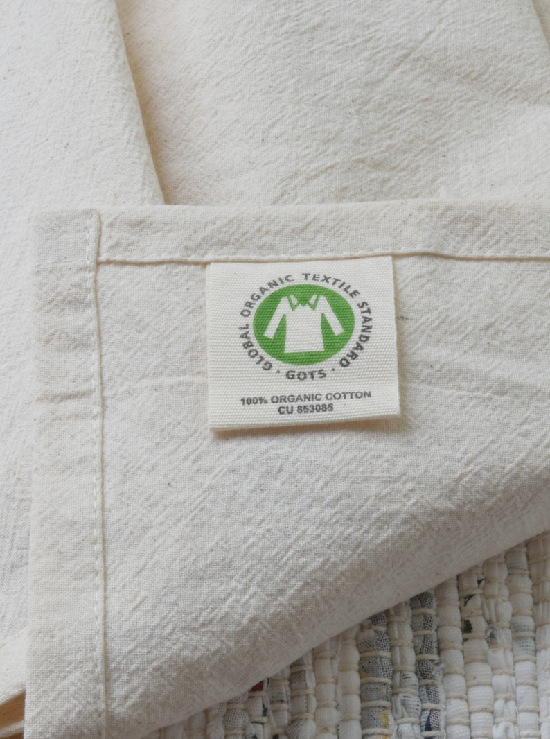 May include: A white fabric label with green text that reads "Global Organic Textile Standard GOTS 100% Organic Cotton CU 853085". The label has a green icon of a shirt inside a circle.
