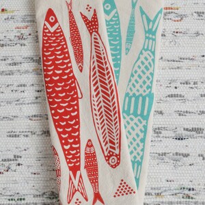 May include: Two white kitchen towels with red and blue fish designs. The fish are stylized and have a folk art feel. The towels are folded and displayed on a white background.