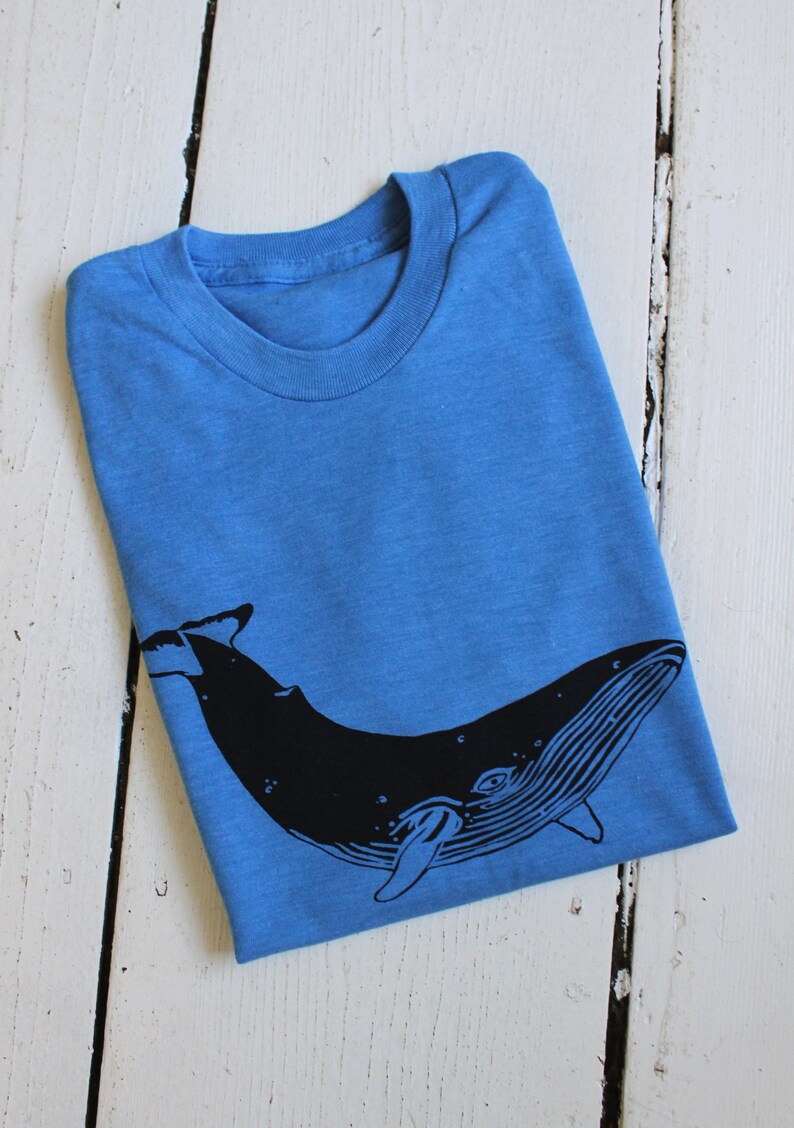 May include: A blue t-shirt with a black whale graphic printed on the front.