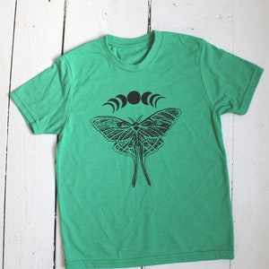 May include: A green t-shirt with a black and white graphic of a moth and a crescent moon design.