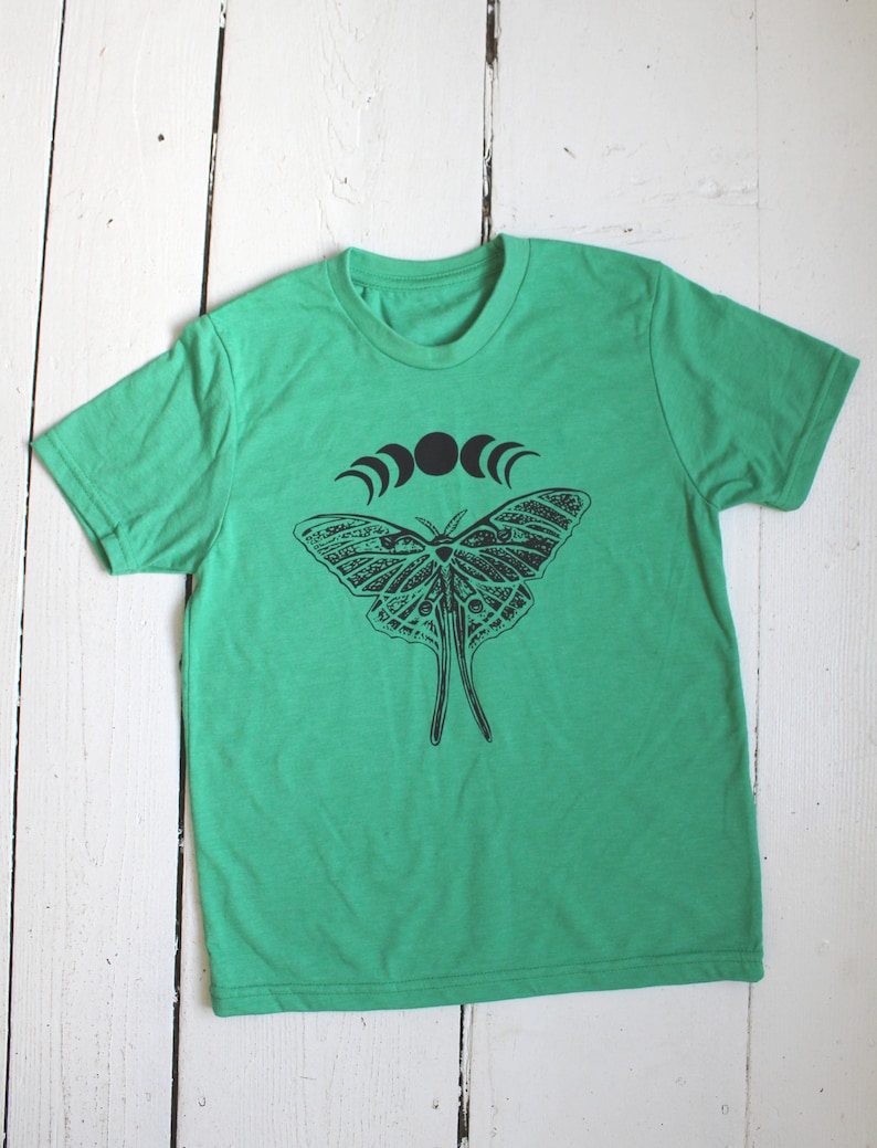 May include: A green t-shirt with a black and white graphic of a moth and a crescent moon design.