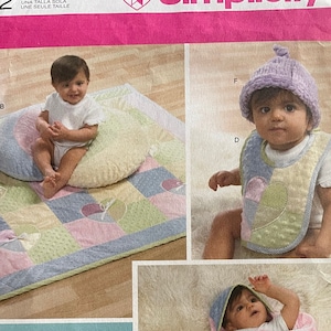 May include: A Simplicity sewing pattern for baby items, including a hooded blanket, a diaper bag, a bib, and a pillow. The pattern is for one size and features a patchwork design with pink, green, and blue colors. The pattern is called "Shirley Botsford Designs" and is for Lion Brand Yarn.