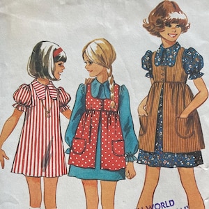 May include: Vintage Simplicity sewing pattern envelope, featuring illustrations of three girls in dresses. The envelope is yellow and white, with the pattern number 5280 and size information. The text "THE CLOTH WORLD ALL PATTERN SALES FINAL NO REFUNDS OR EXCHANGES" is also visible.