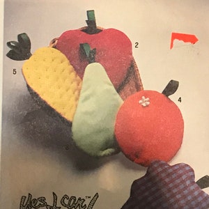 May include: Simplicity sewing pattern number 9304 for making fruit-shaped plush toys. The pattern includes instructions for beginners and features a red apple, a yellow pear, a green pear, and a red orange. The pattern also includes a blue and white checkered fabric for a separate project.