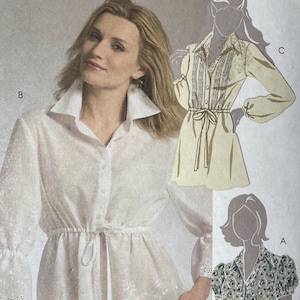 May include: McCall's sewing pattern M5470 featuring three blouse designs. The pattern includes a white eyelet blouse with a tie waist, a cream-colored blouse with lace detailing, and a floral print blouse. Size A5 (6-8-10-12-14).