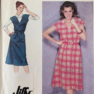 May include: Simplicity sewing pattern number 9423 for a dress. The pattern is for size 12 miss. The pattern shows two models wearing the dress. One model is wearing a blue dress with a white collar and a belt. The other model is wearing a pink and white plaid dress with a V-neck.