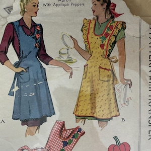 May include: Vintage McCall's sewing pattern for aprons, featuring illustrations of women wearing different apron designs. The pattern includes applique pepper details and the text "Ladies' and Misses' Apron With Appliqué Peppers". The pattern is in a plastic sleeve.