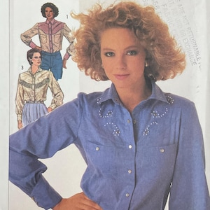 May include: Simplicity sewing pattern 7231. The pattern features a woman wearing a light blue button-down shirt with decorative embellishments. The pattern includes sizes 10, 12, and 14. The image also shows illustrations of the shirt.