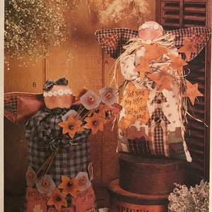 May include: A McCall's Crafts pattern for making two fabric angels. The angels are dressed in plaid and floral fabric and have a rustic, country style. The pattern is number 8441.